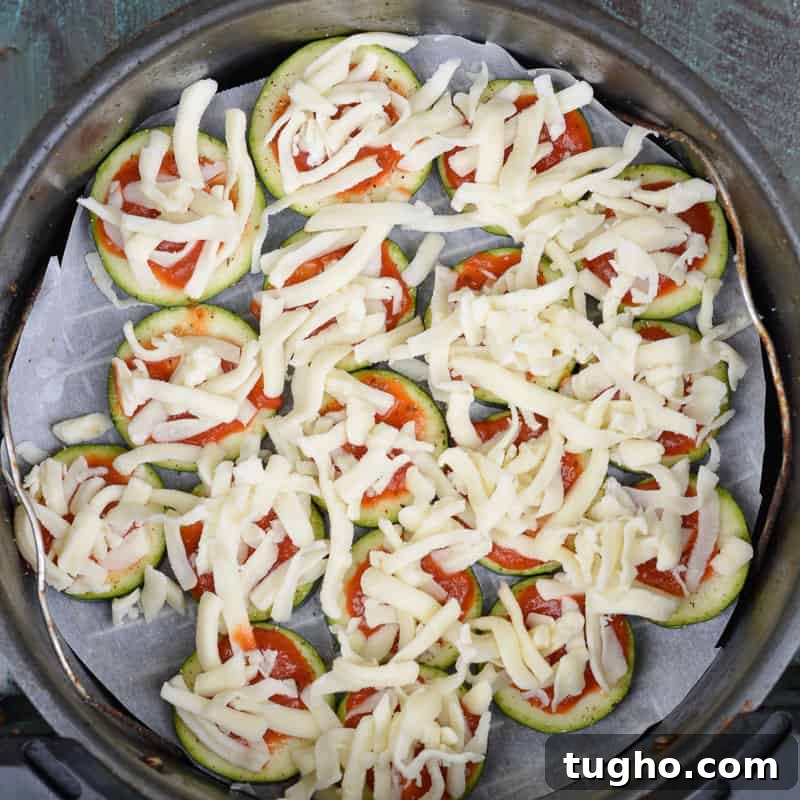 Zucchini pizza bites topped with shredded cheese before air frying