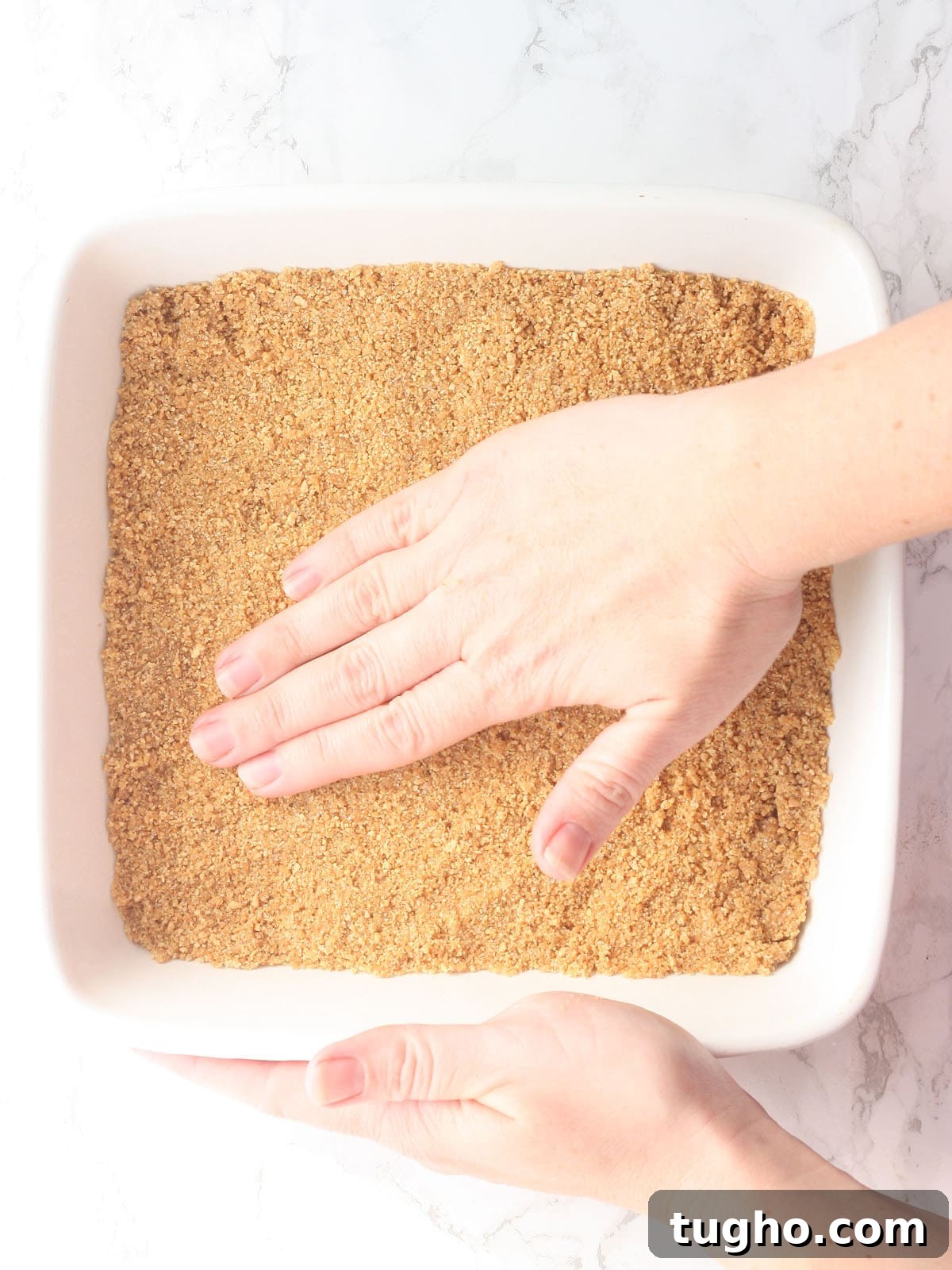 hand pressing graham cracker crumbs into the bottom of an 8 x 8-inch baking dish