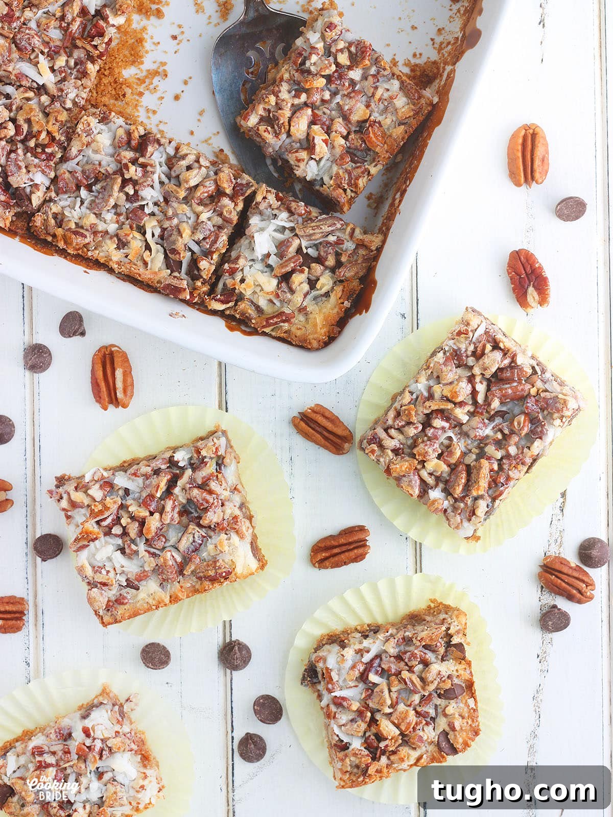 Over head shot of four Hello Dolly Bars on yellow wrappers surrounded by chocolate chips, pecans and a pan of cut bars to the side