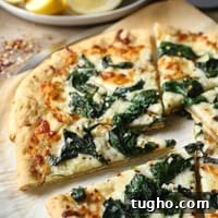 Spinach Garlic White Pizza 6 White pizza with spinach and garlic on parchment paper with lemon wedges