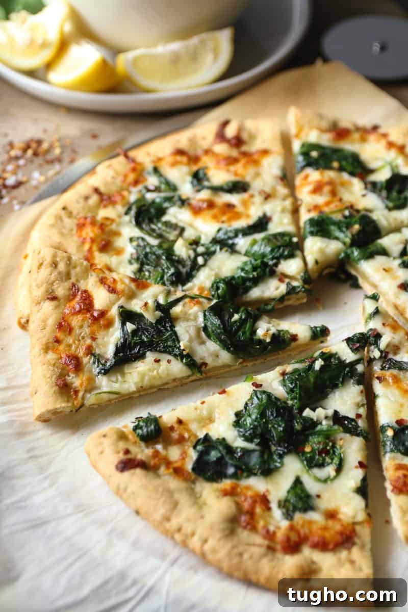 Spinach Garlic White Pizza 7 White pizza with spinach and garlic on parchment paper with lemon wedges