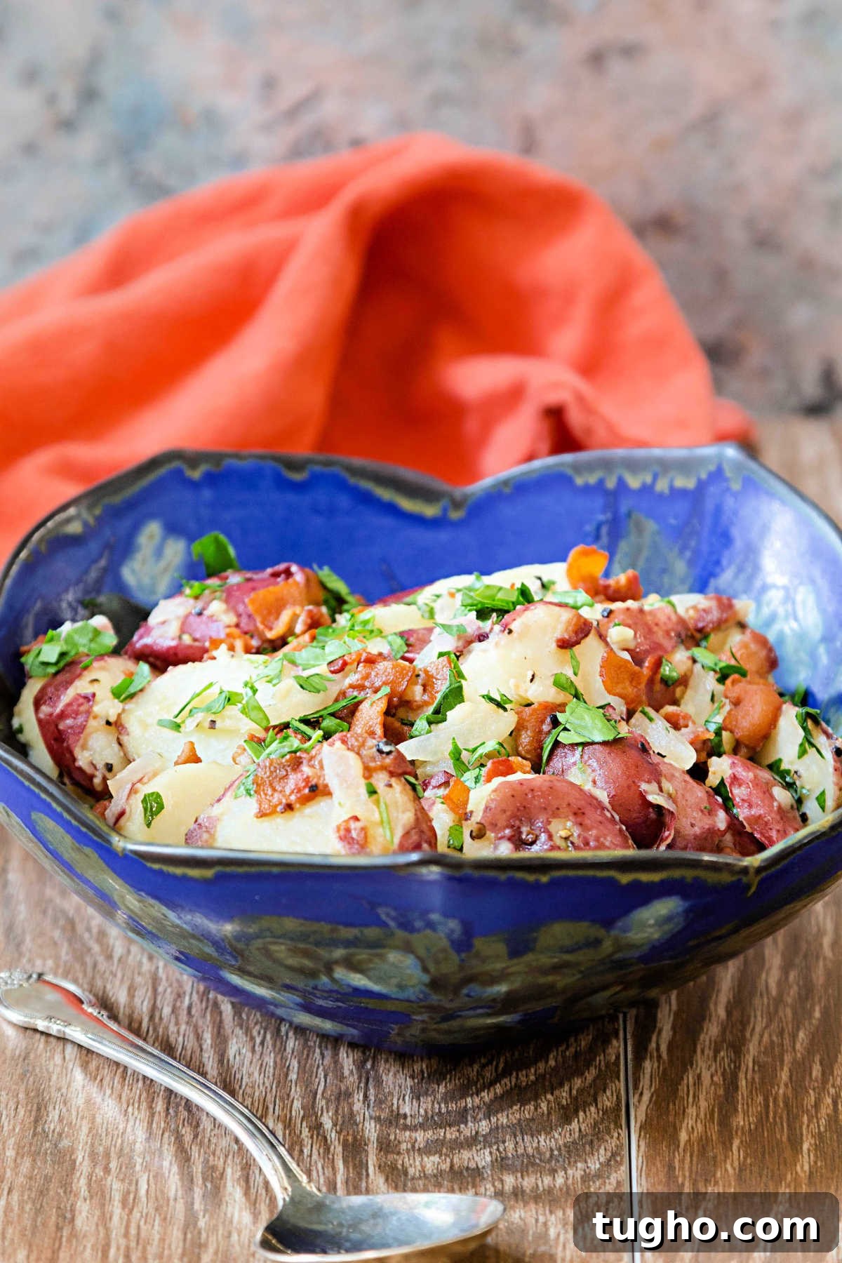 Authentic Warm German Potato Salad Recipe 2 A blue serving bowl of German potato salad with bacon and parsley.