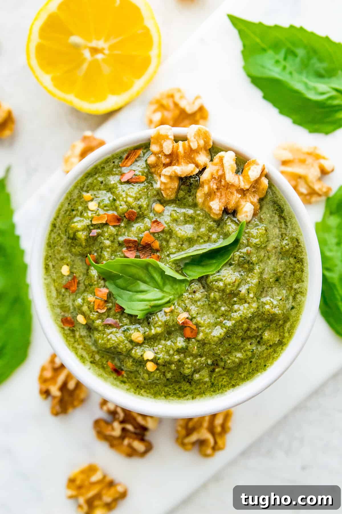 A bowl of walnut pesto topped with walnuts and fresh basil leaves.