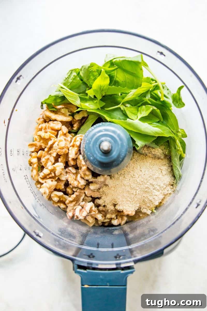 A food processor filled with walnuts, basil leaves and nutritional yeast.