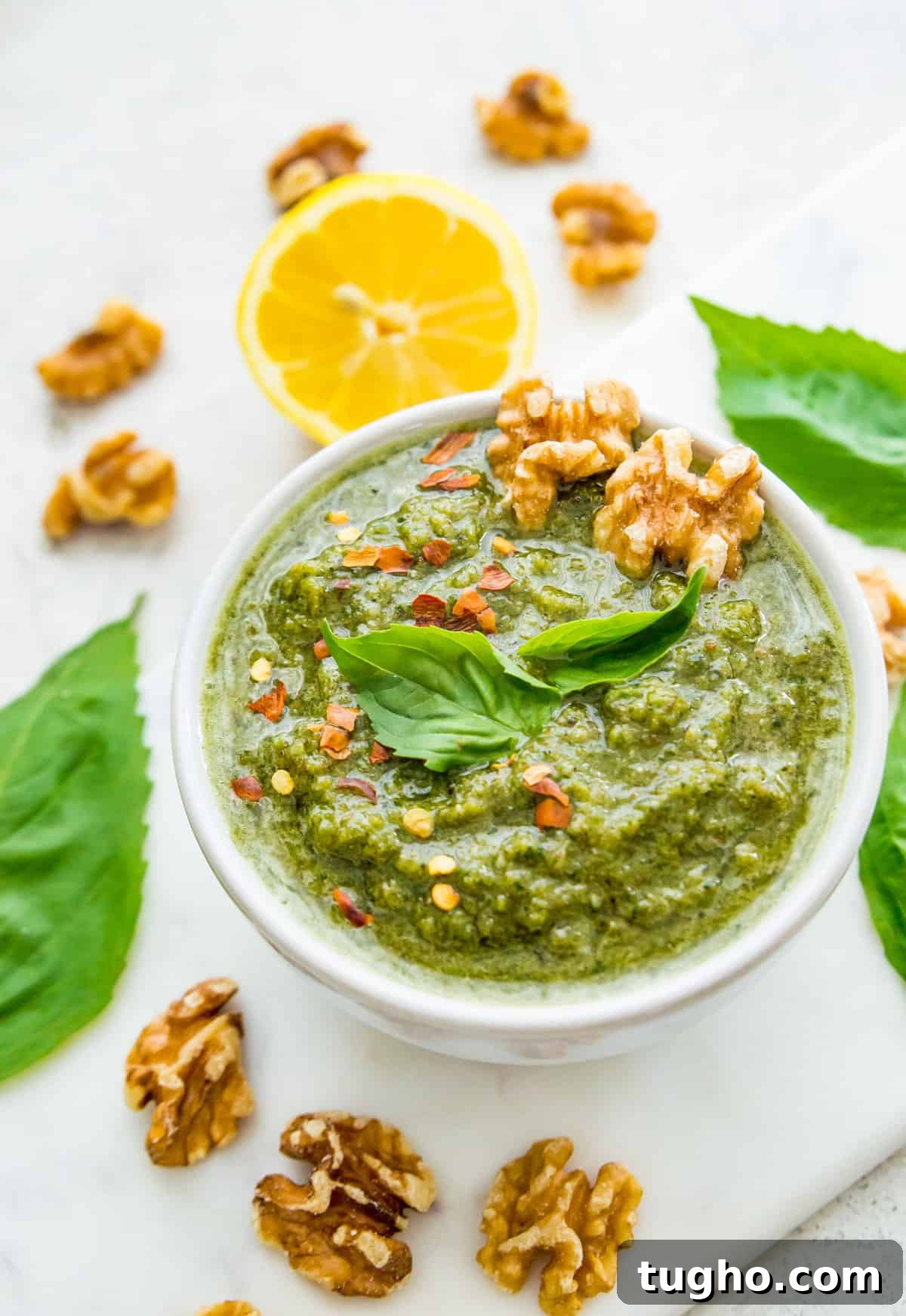 A bowl of green pesto topped with walnuts and fresh basil leaves.