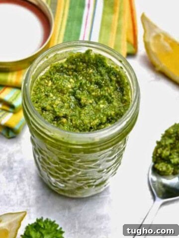 A glass jar filled with a green pesto sauce with a lemon wedge next to the jar.