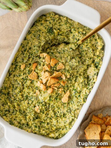 A white casserole dish filled with a vegan spinach artichoke dip with crushed crackers on top.