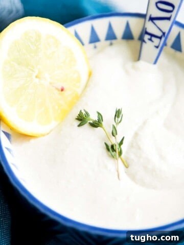 A bowl of dairy free sour cream with a spoon in it and a lemon slice on top.