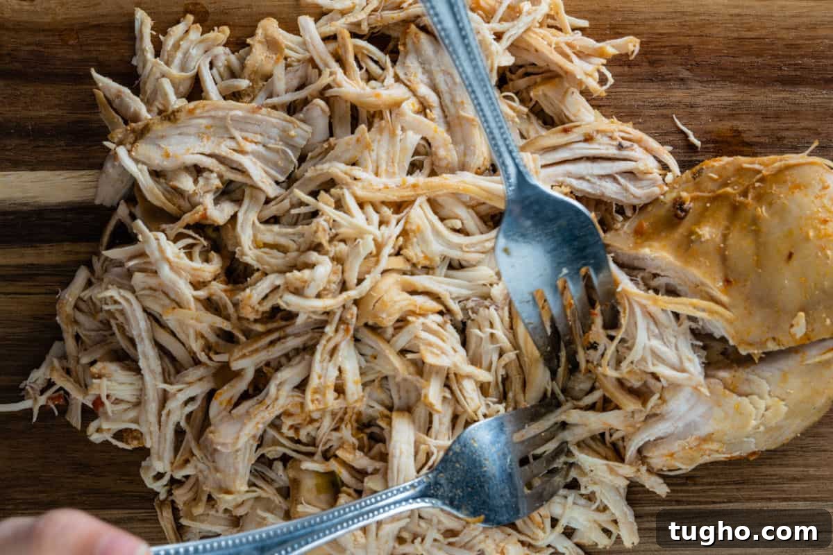 Instant Pot Chicken Stew with Tender Vegetables 8 Shredding chicken on a cutting board with two forks.