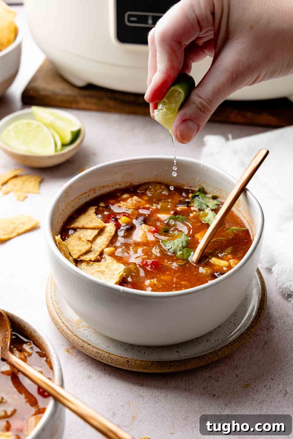Slow Cooker Chicken Tortilla Soup Recipe 2 Hand squeezing lime juice into bowl of chicken tortilla soup garnished with tortilla chips.