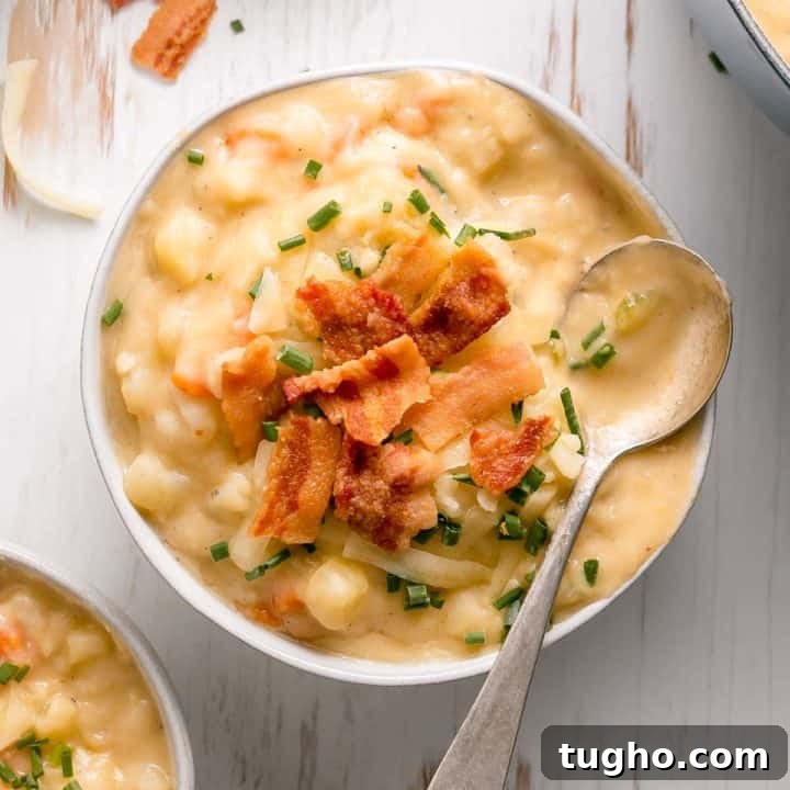 A bowl of creamy gluten-free potato soup topped with bacon, white cheddar cheese, and chives.