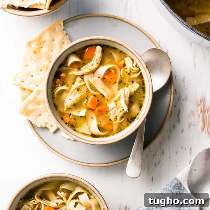 A bowl of gluten free chicken noodle soup shown from above with crackers and a spoon to the side.