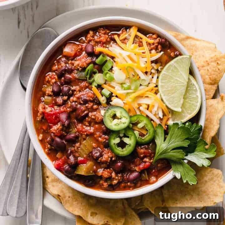 A bowl of chili garnished with cheese, jalapenos, green onion, and lime wedges.