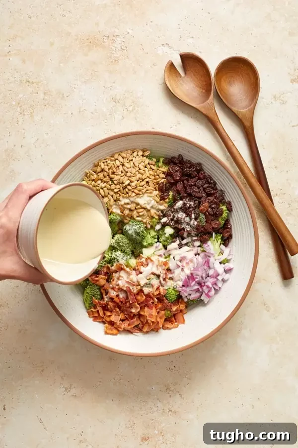 Dairy-Free Broccoli Salad Recipe with Cranberries and Almonds 4 Someone pouring dressing into a bowl of broccoli salad.