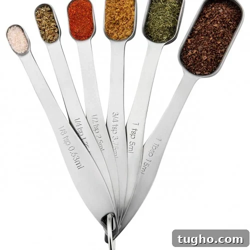 A set of six metal measuring spoons, each filled with a different spice.