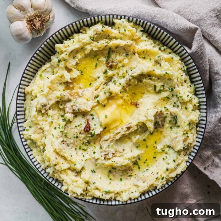 Roasted garlic yukon mashed potatoes with parmigiano-reggiano, sour cream, creamy roasted garlic, and chives in a striped blue and white bowl.