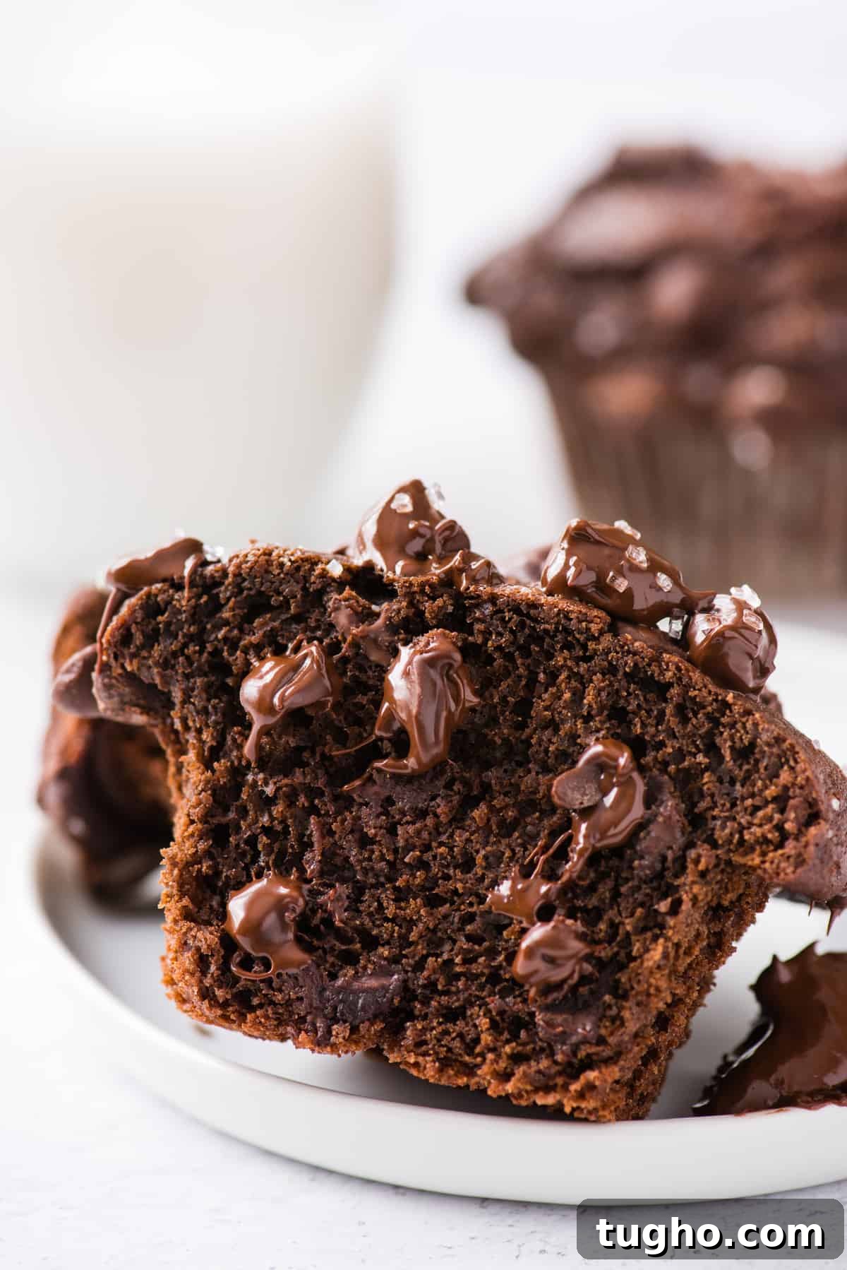 a double chocolate chip muffin cut in half showing melty chocolate chips inside on white plate on white background