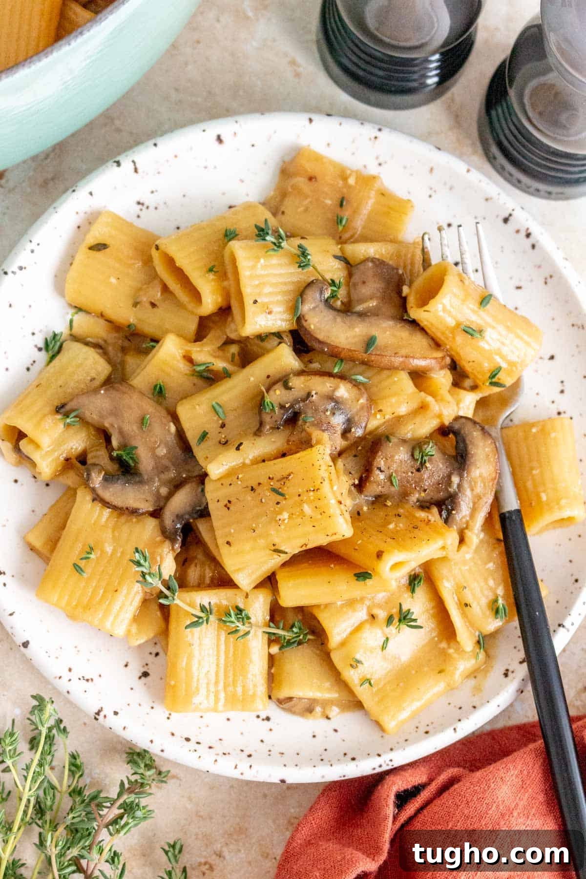 Creamy One-Pot French Onion Pasta 2 A plate of french onion pasta with a fork garnished with fresh thyme.