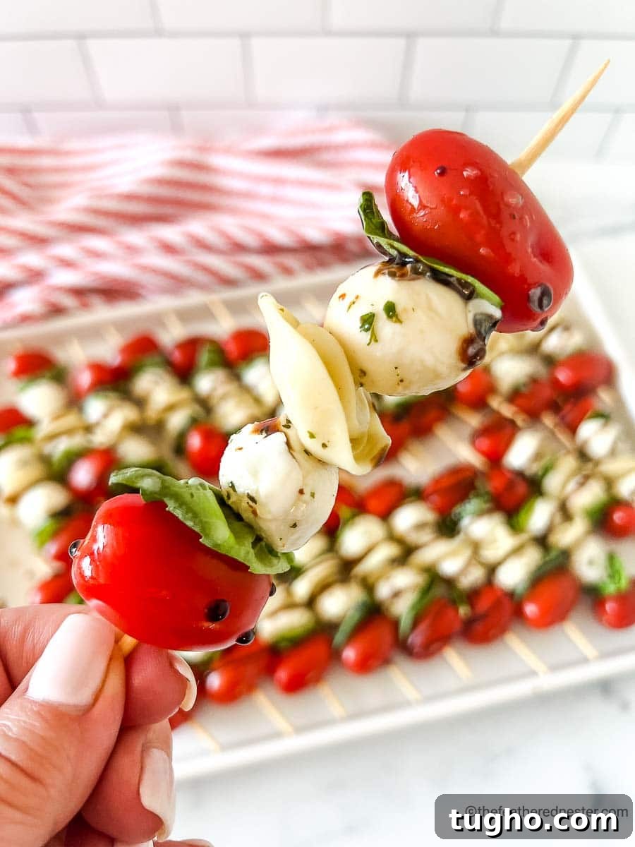 a closeup of a caprese kabobs with a tray of caprese skewers with balsamic glaze and a red and white napkin in the background.