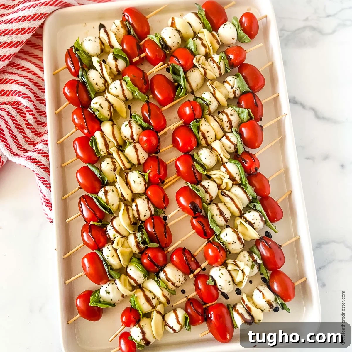 a white tray of kabob party appetizers with balsamic glaze on top of a red and white napkin.