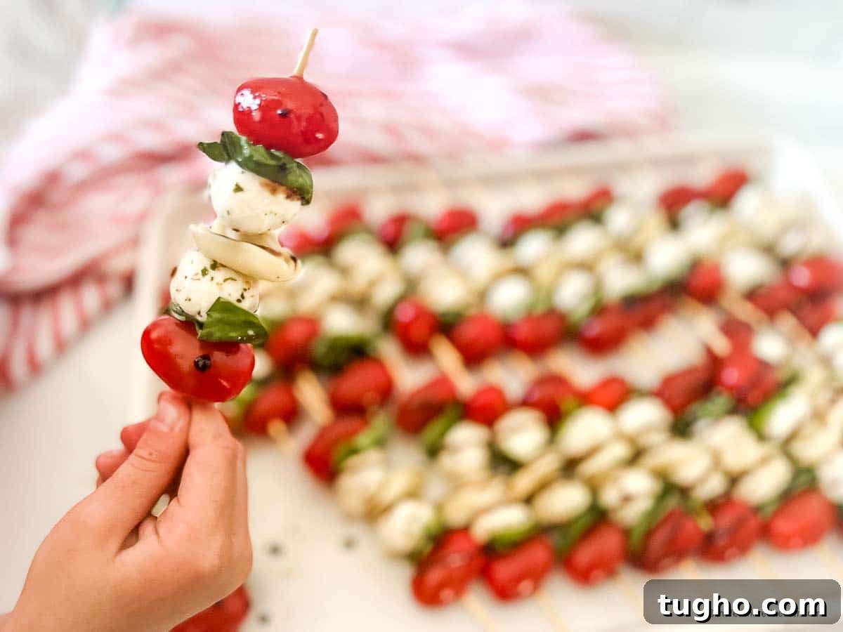 a closeup of a caprese tortellini appetizer with a tray of caprese skewers with balsamic drizzle and a red and white napkin in the background