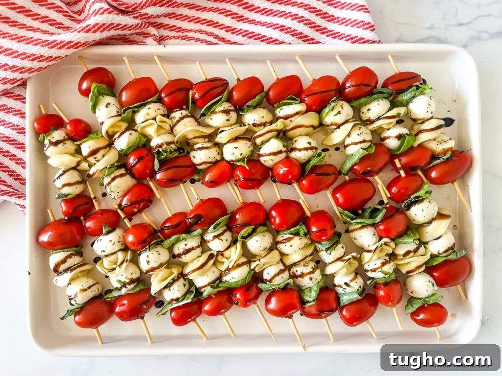 a white tray of tortellini skewers with balsamic glaze on top of a red and white napkin