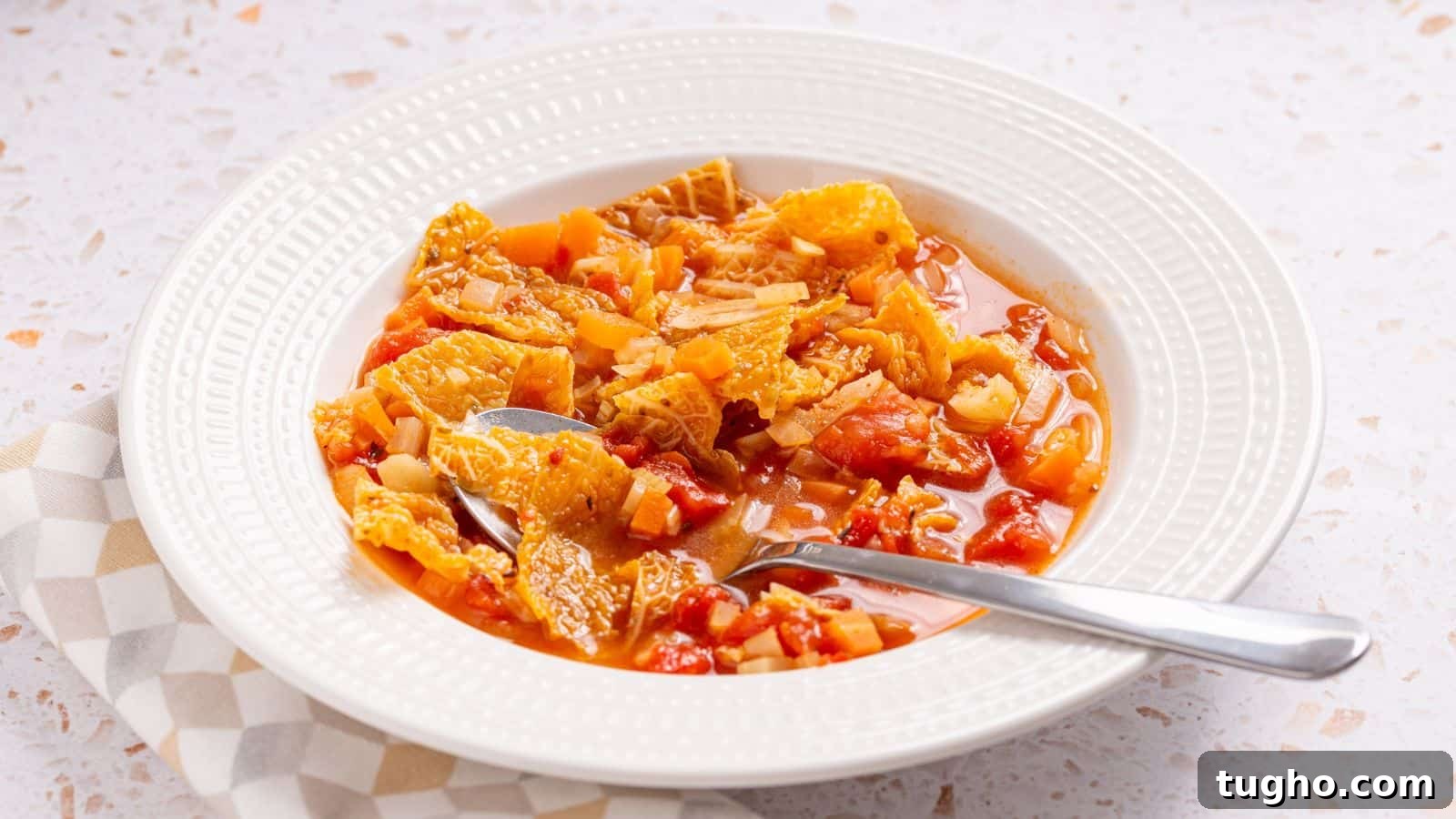 Bowl of hearty vegetable soup with a spoon on a checked napkin.