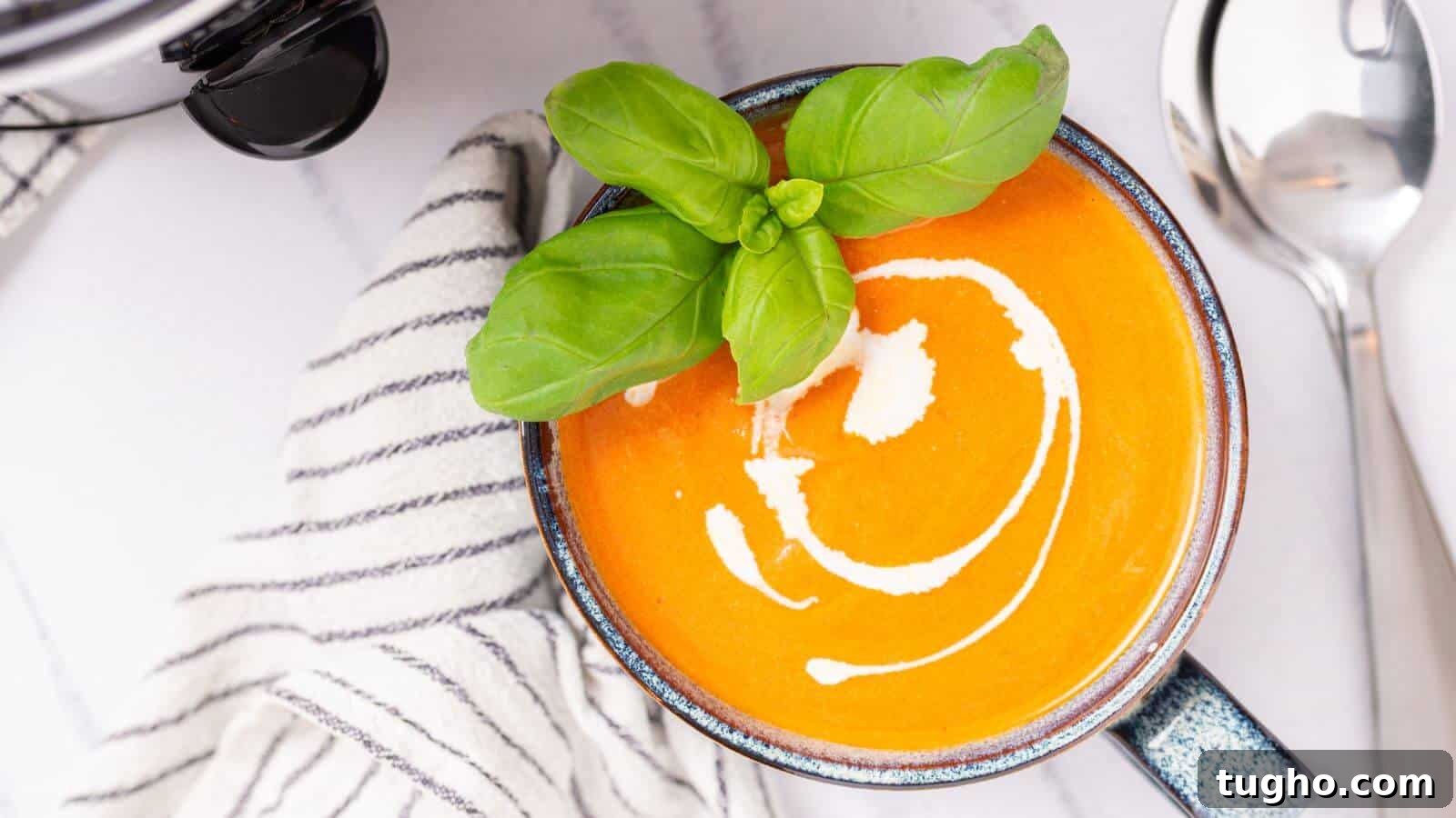 Top view of a bowl of creamy tomato soup garnished with basil, served with a spoon and sunglasses on the side.