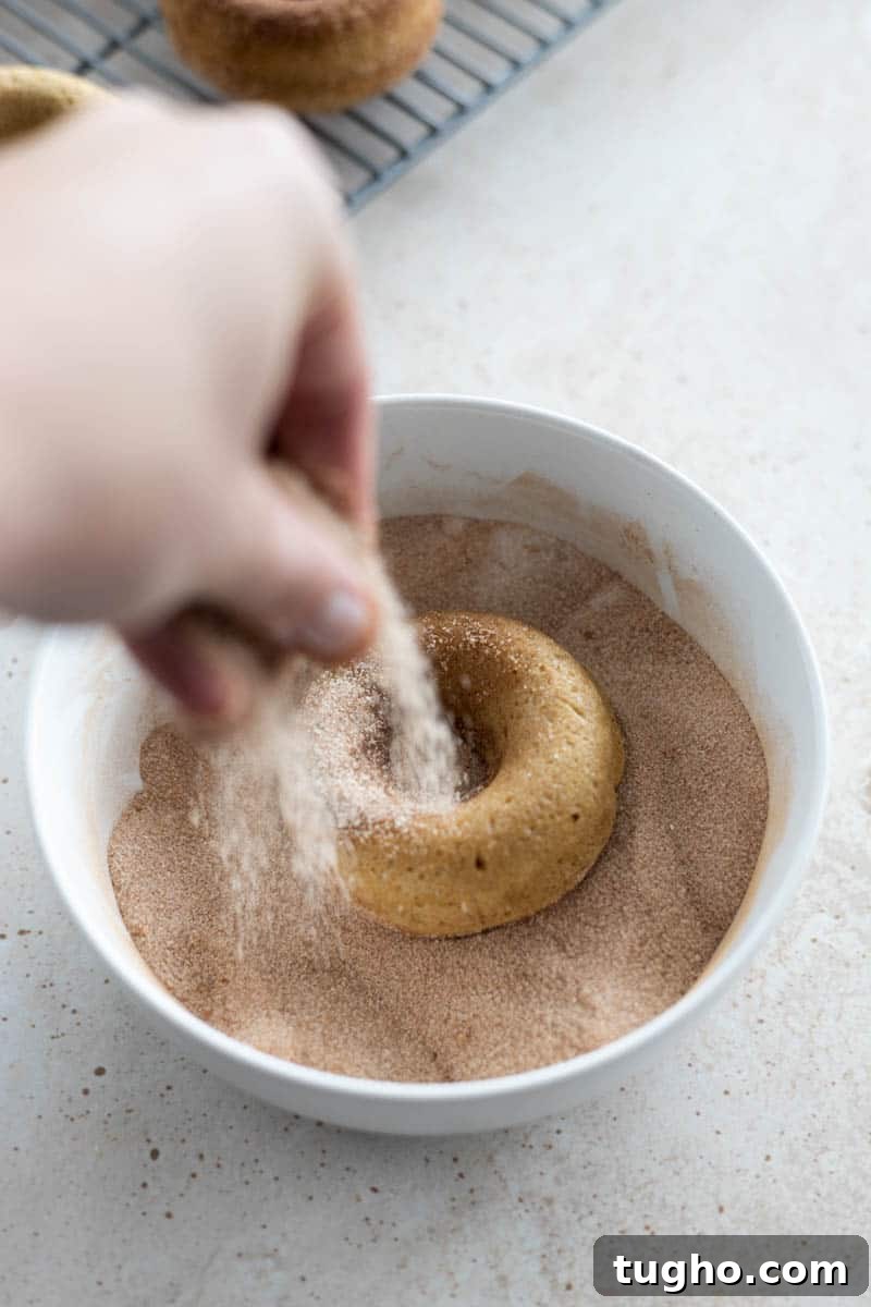 Homemade Baked Cinnamon Sugar Donuts Recipe 10 Sprinkling a donut with cinnamon sugar in a bowl.