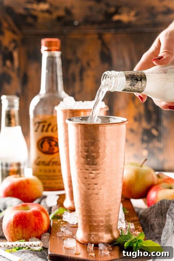 This apple cider Moscow mule puts a fall spin on a classic cocktail! Served in a copper mug, garnished with a cinnamon stick and apple slice. Ginger beer being poured into a copper mug.