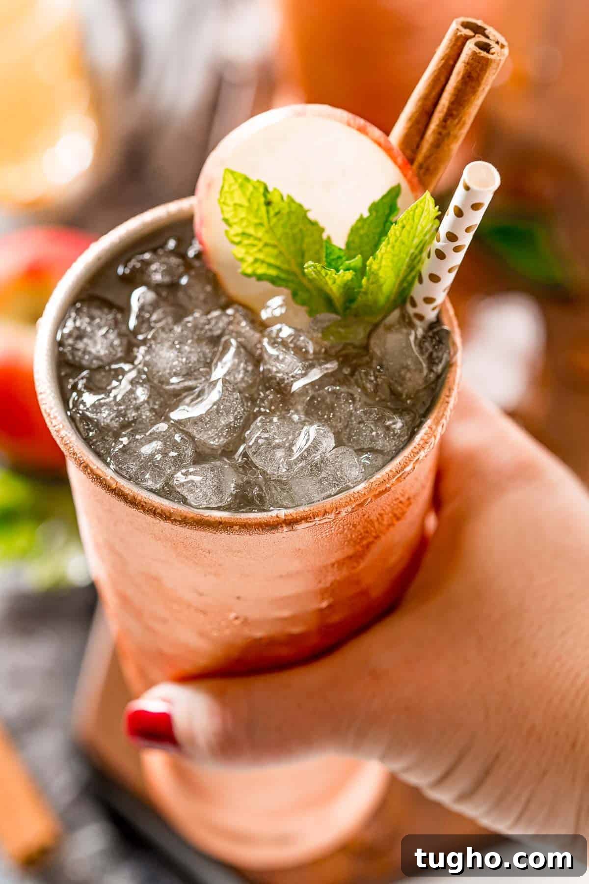 This apple cider Moscow mule puts a fall spin on a classic cocktail! Served in a copper mug, garnished with a cinnamon stick and apple slice. Apple cider moscow mule in a woman's hand.
