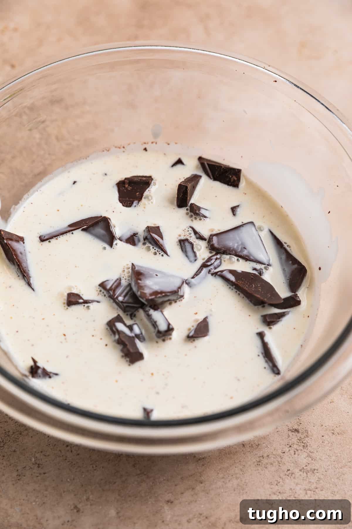 Warm cream poured over dark chocolate in mixing bowl