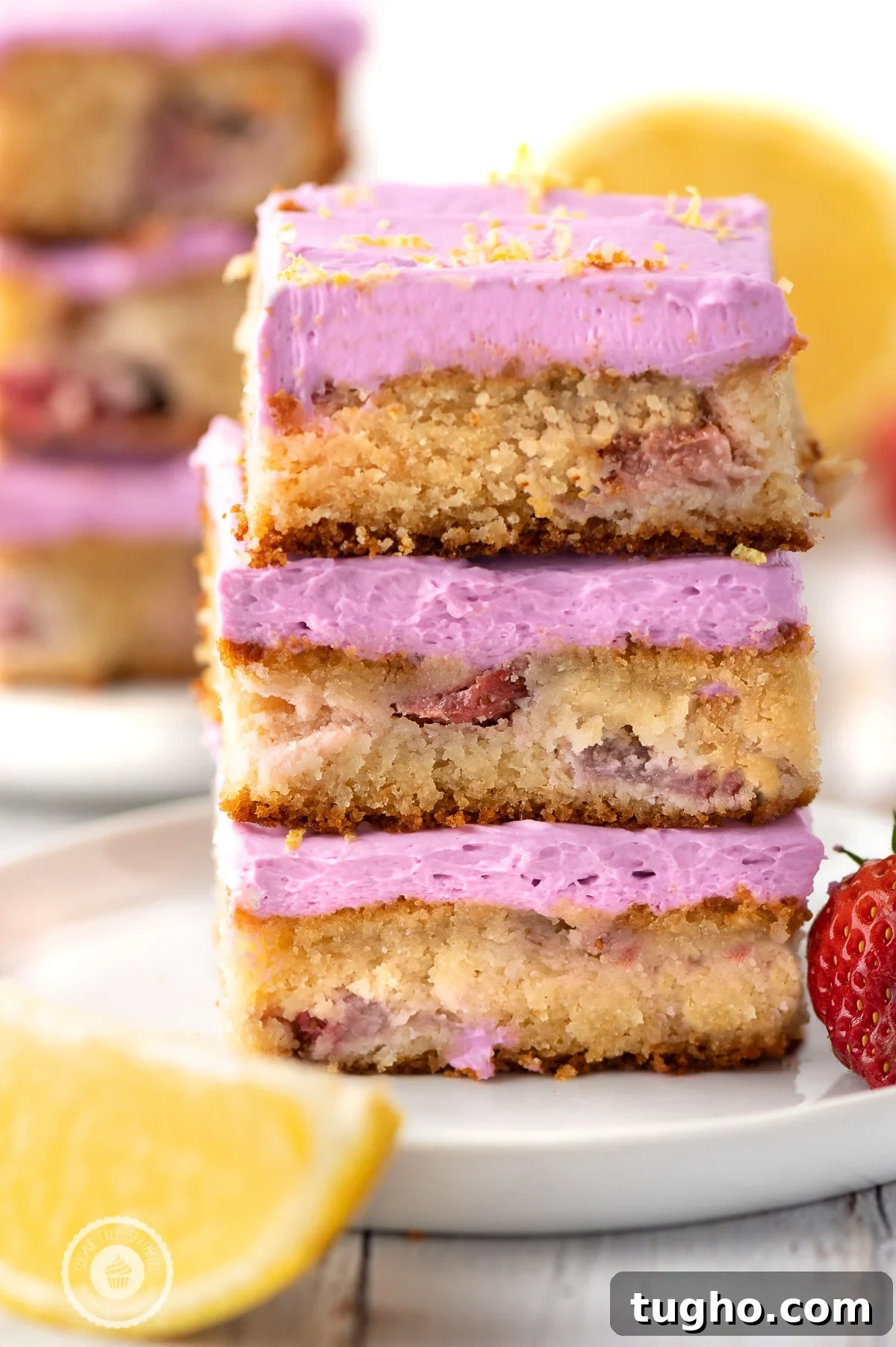 Low-Carb Strawberry Lemon Blondies, Keto and Gluten-Free 2 Three stacked low carb strawberry lemon blondies with pink frosting on a white plate with lemon wedges and strawberries .
