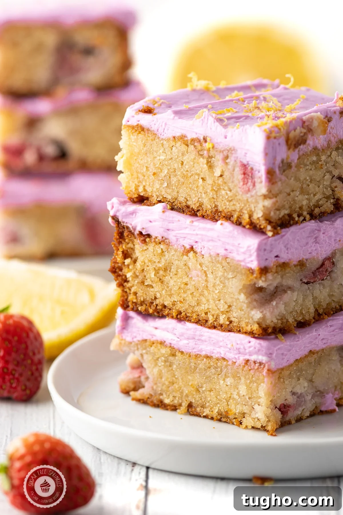 Low-Carb Strawberry Lemon Blondies, Keto and Gluten-Free 3 Three stacked low carb strawberry lemon blondies with pink frosting on a white plate with lemon wedges and strawberries .