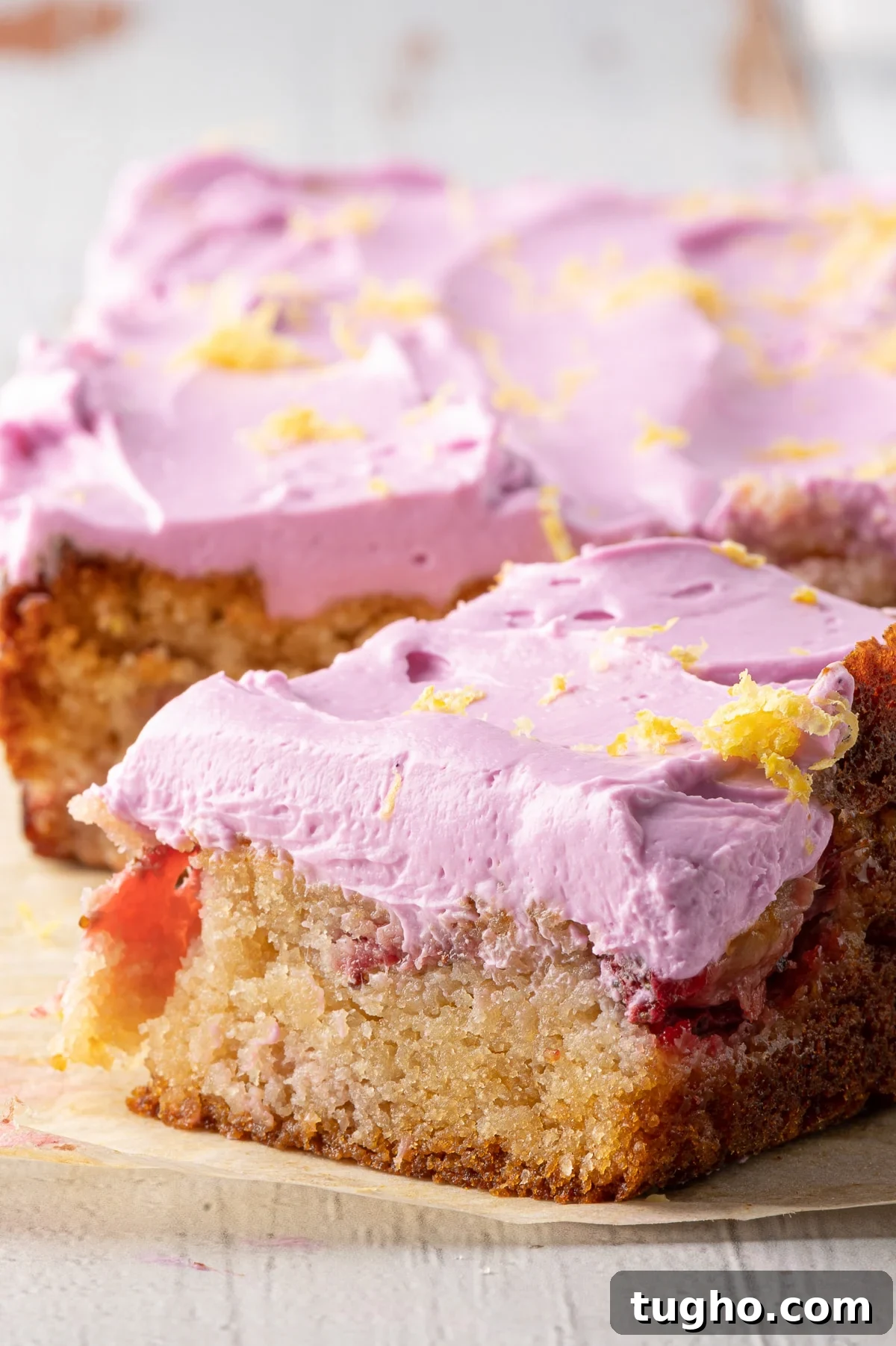 Low-Carb Strawberry Lemon Blondies, Keto and Gluten-Free 5 A golden blondie with bits of strawberry and pink icing on a piece of parchment paper