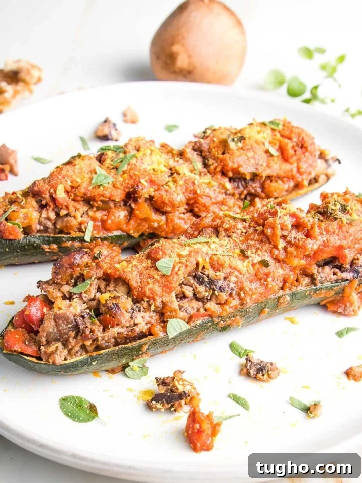 Rimmed white plate with 2 zucchini boats, stuffed with mushrooms and other chopped veggies.