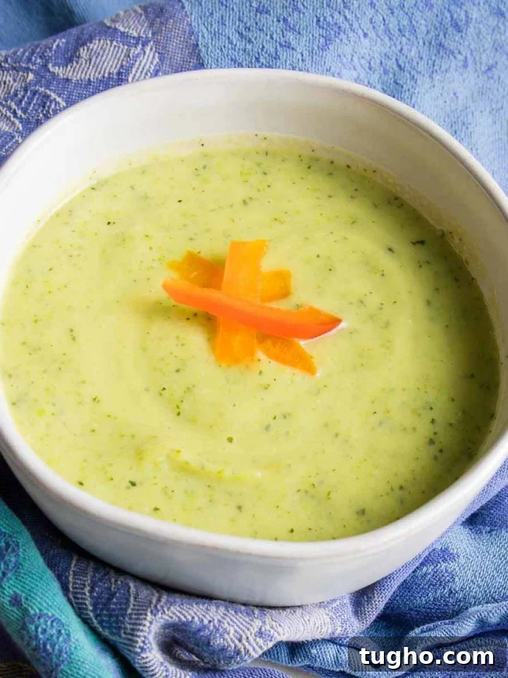 Light green creamy soup with red pepper slices as garnish.