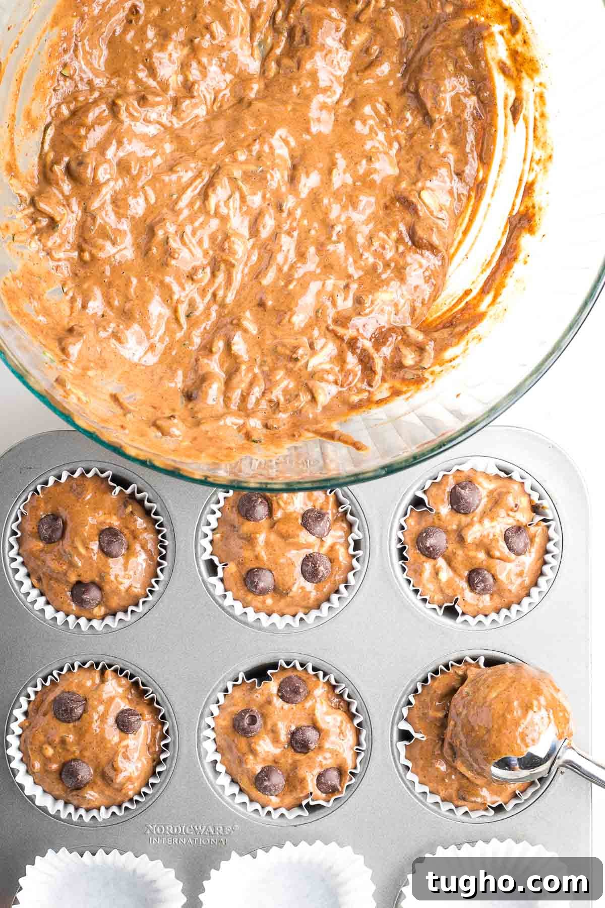 Fudgy Double Chocolate Zucchini Muffins Recipe 10 Bowl of muffin batter being scooped into lined muffin tins and the muffins are topped with chocolate chips.