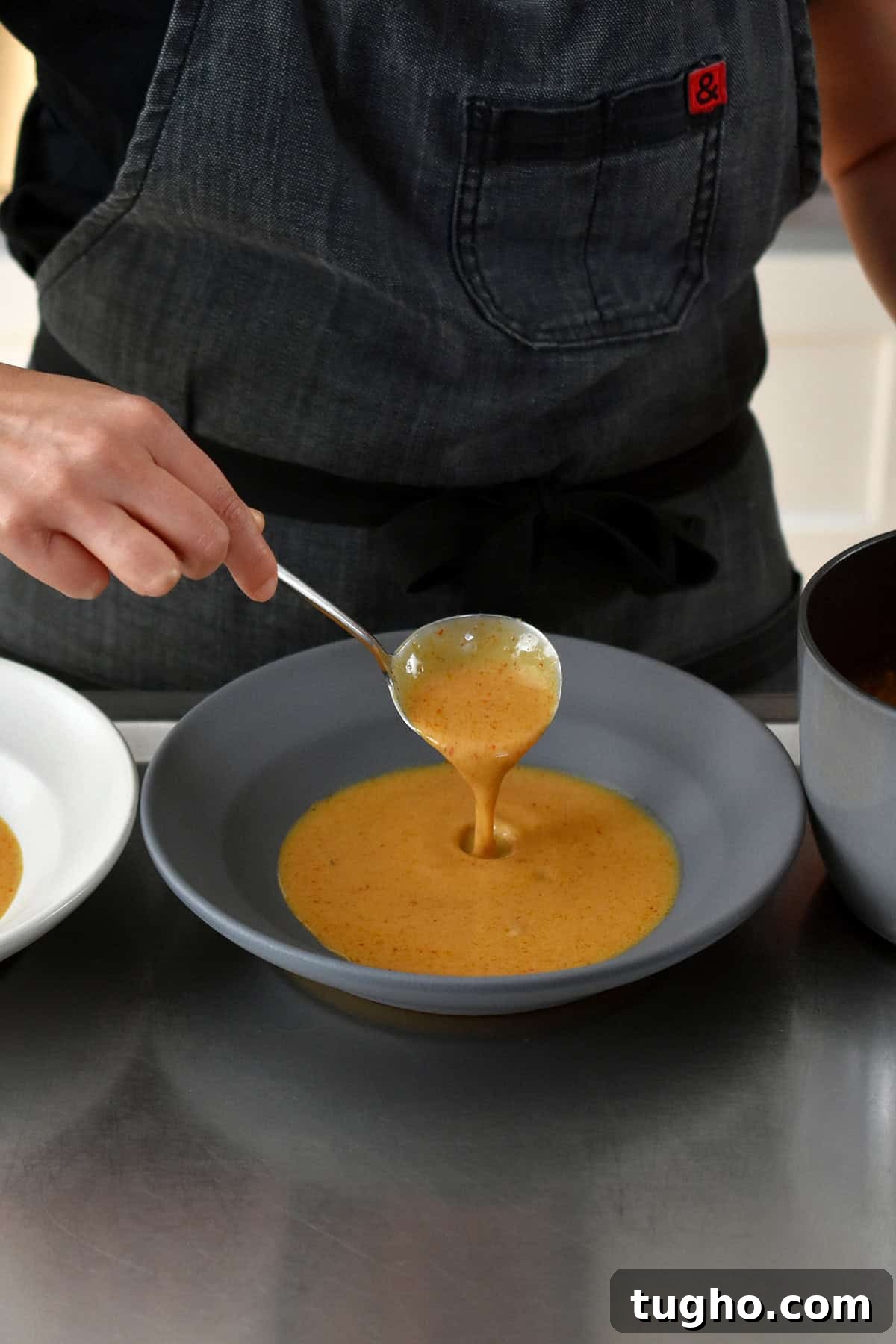 Spooning homemade Thai red curry sauce into a shallow gray bowl before placing a baked lobster tail on top.