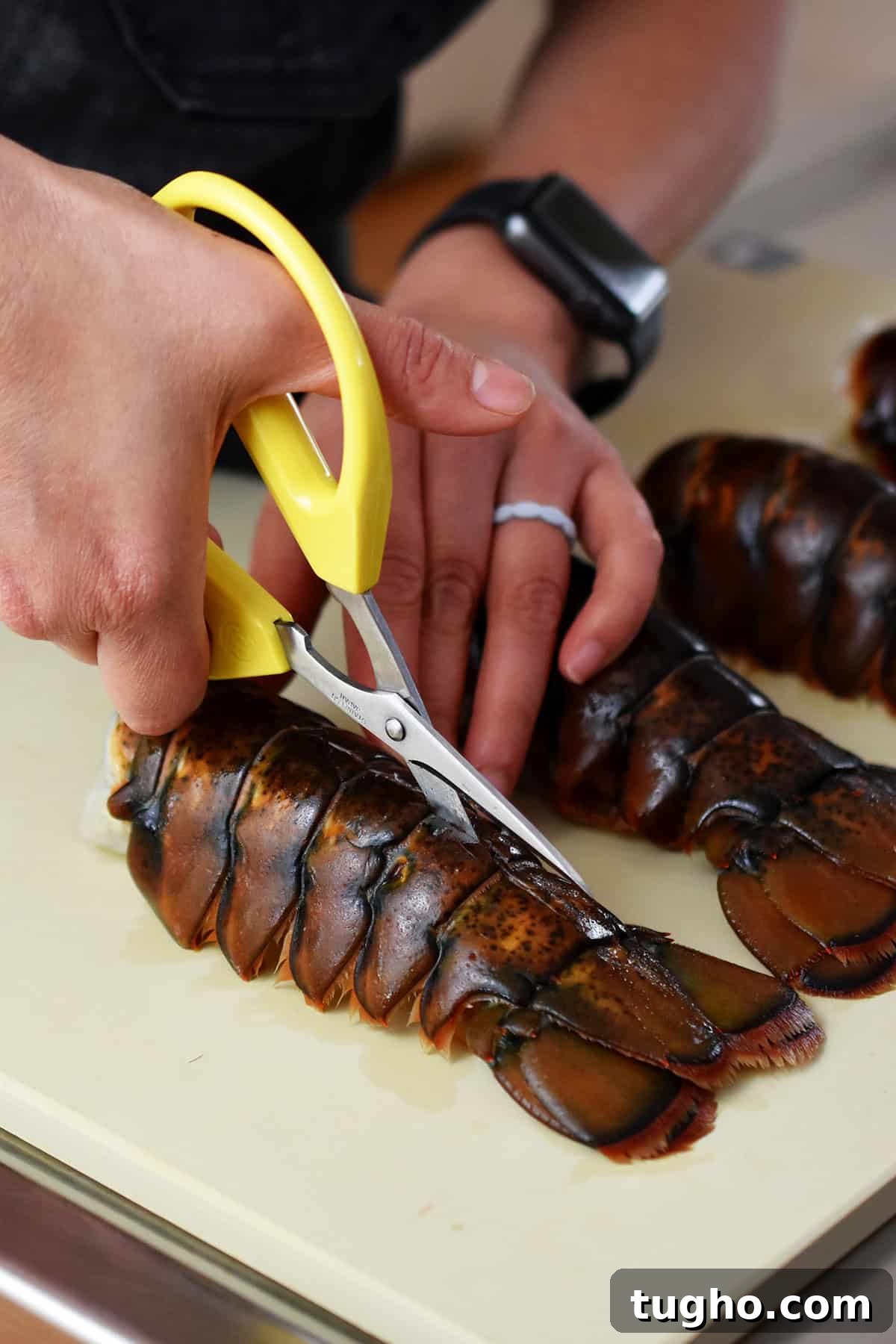 Using a pair of yellow kitchen shears to cut a line in the top of the shell of a raw lobster tail.