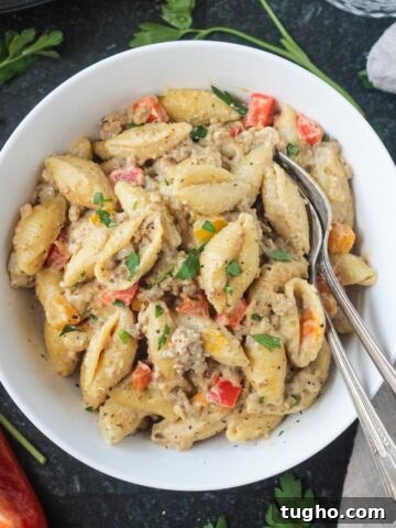 Creamy vegan beef pasta with peppers in a white bowl with two forks.