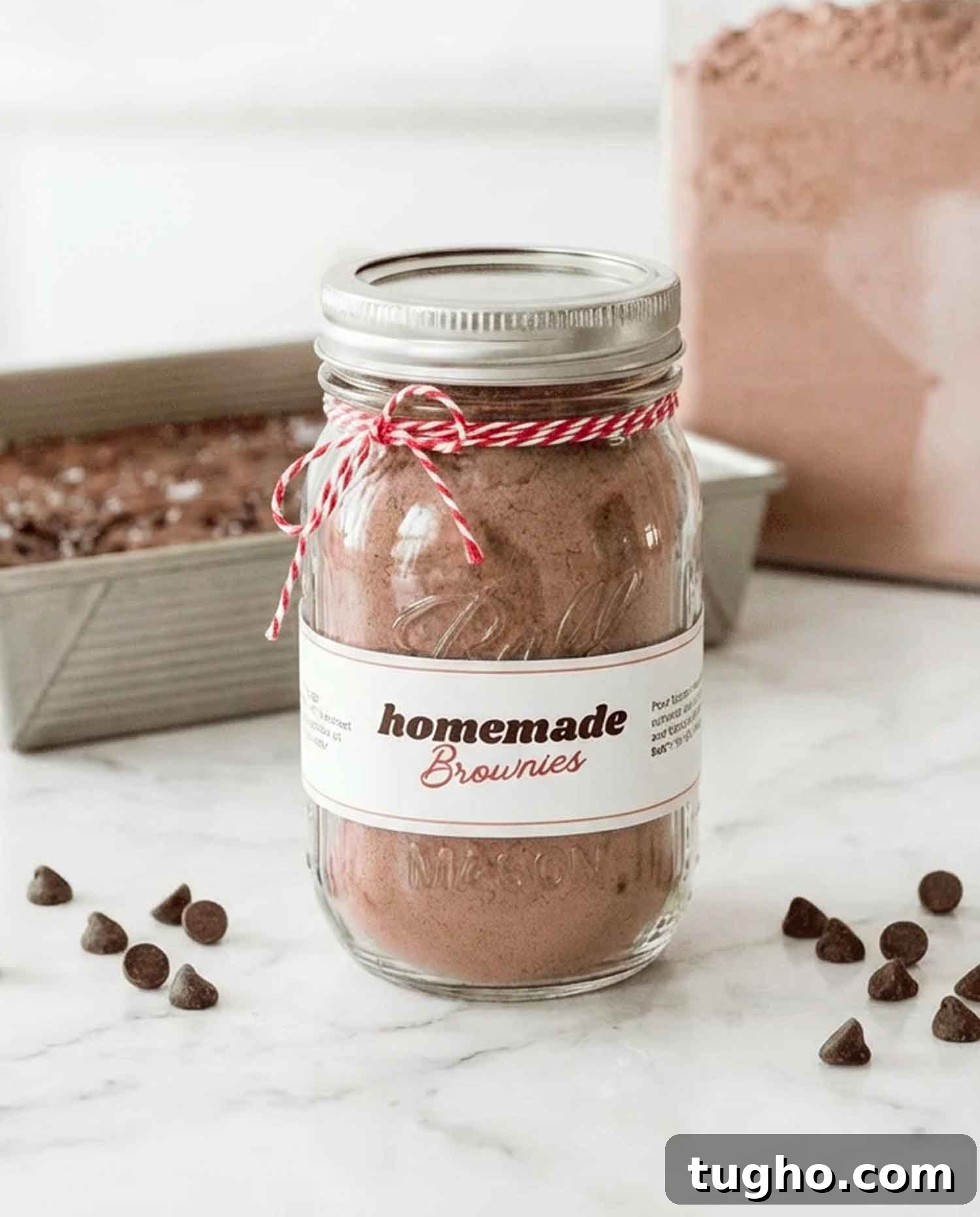 Homemade Brownie Mix Recipe for Gifts 2 Homemade brownie mix in a mason jar tied with red and white twine, with a printable label and chocolate chips scattered on a white marble surface