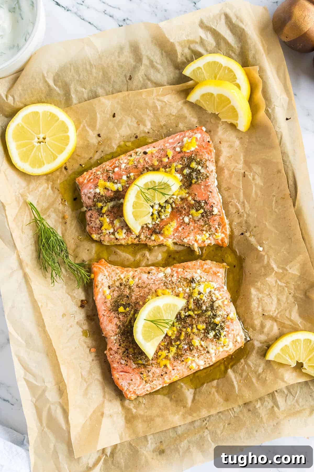 Lemon Dill Salmon Recipe 2 Two baked salmon fillets on parchment paper with lemon wedges and sprigs of dill.