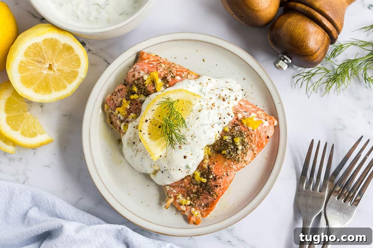 Lemon Dill Salmon Recipe 5 Baked salmon topped with lemon dill sauce on a white plate with lemon wedges on the side.