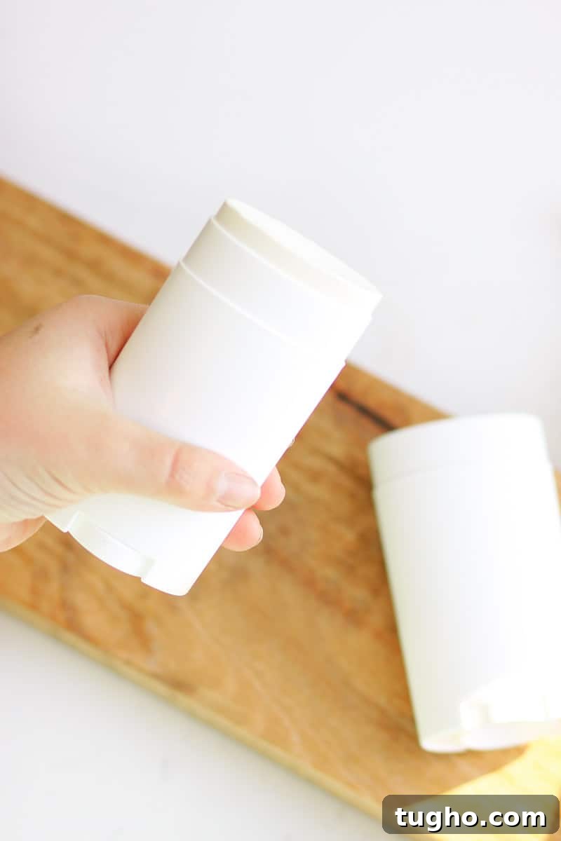a person holding an unused tube of homemade deodorant with another tube laying on a countertop behind it