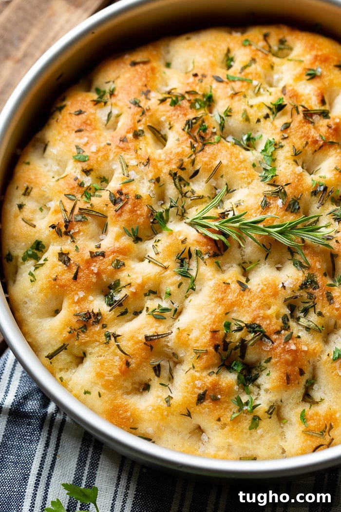 No-Knead Herbed Focaccia with Rosemary and Sea Salt 4 Round focaccia loaf topped with herbs and flaky salt in a silver pan