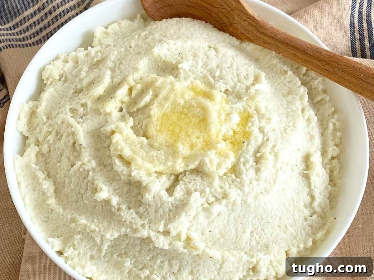 15 Make-Ahead Thanksgiving Recipes to Prep Now 4 White bowl with mashed cauliflower with pooled butter in the center and a wooden spoon.