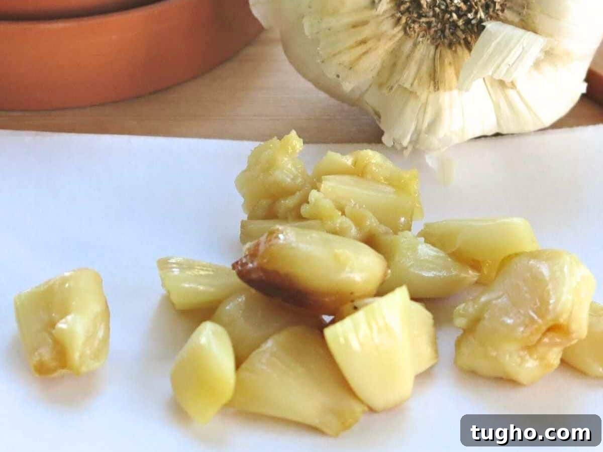 15 Make-Ahead Thanksgiving Recipes to Prep Now 10 Roasted garlic cloves on parchment paper with a whole garlic clove behind them.