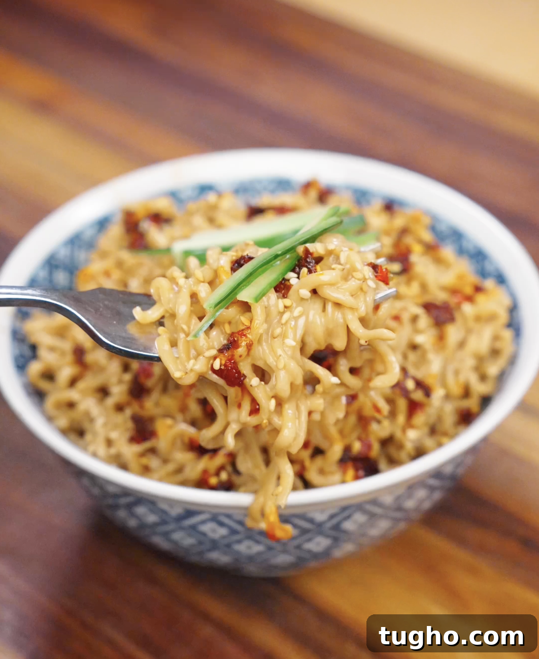 Creamy Sesame Noodles with Garlic Soy Sauce 3 Fork lifting creamy sesame noodles topped with chili oil, sesame seeds, and cucumber garnish.