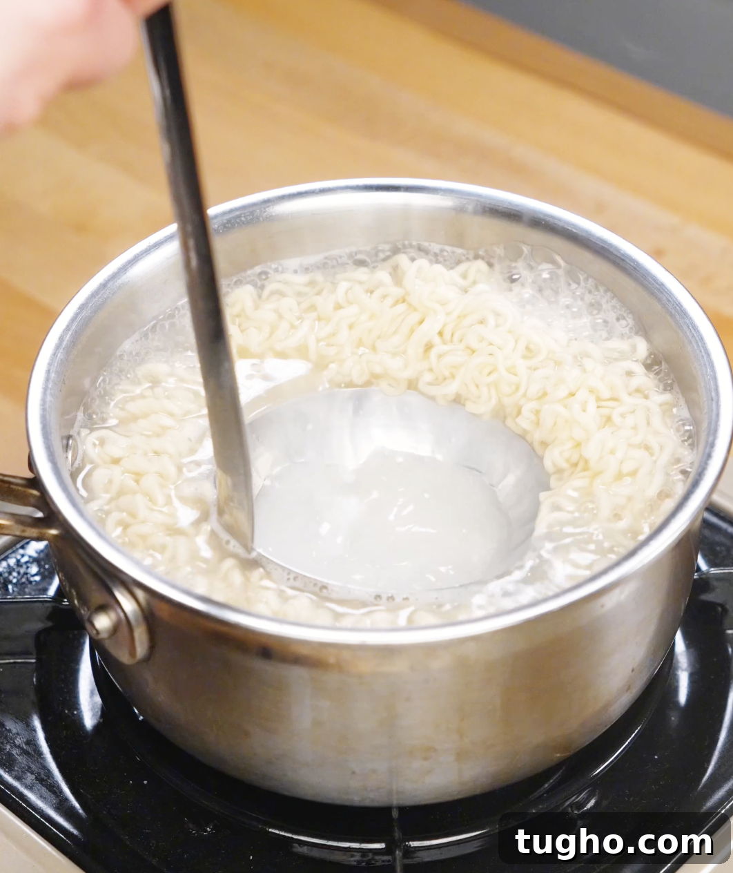 Creamy Sesame Noodles with Garlic Soy Sauce 5 Ladle scooping starchy noodle cooking water from a pot of boiling ramen.